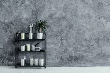 Black industrial shelf with cans and plant on grey concrete wall, real photo with copy space
