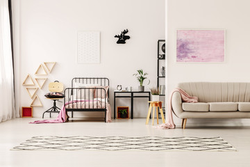 Abstract pastel pink painting above beige stylish couch in scandinavian design kid's bedroom