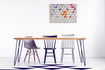 Geometric graphic on white empty wall behind long wooden table with chairs