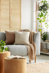 Urban jungle in natural living room with beige pillows on grey couch and open book on wooden table