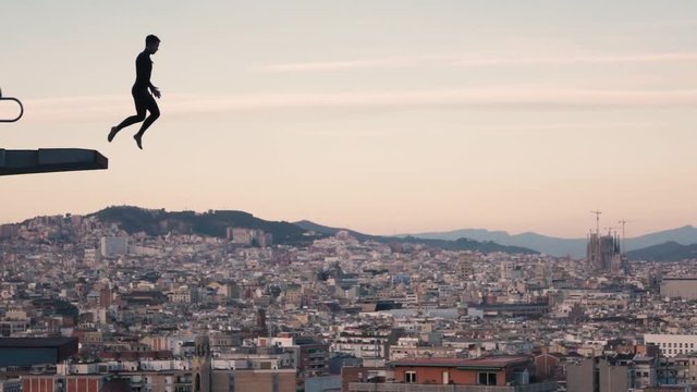 Dark-skinned boy with black neoprene practicing Olympic jump at sunset in the city of Barcelona