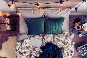 Top view of comfortable king size bed with emerald green pillows, fury duvet and closed laptop