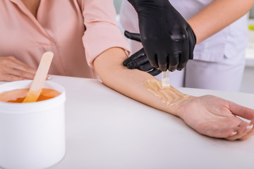 Woman wearing beige blouse having wax depilation on her arm