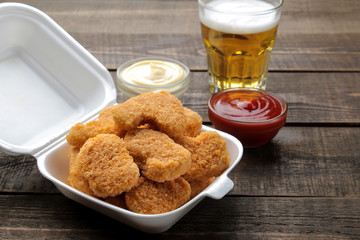 chicken nuggets in a food delivery box with white and red sauce and beer on a brown wooden background. fast food
