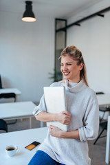 Portrait of a smiling young blonde woman holding laptop computer indoors.