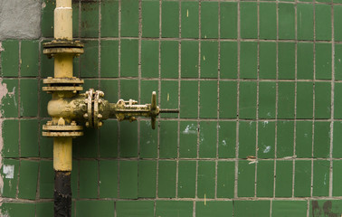 Old weathered gas crane and pipe on the background of a green wall. Old gas gate of yellow colour...