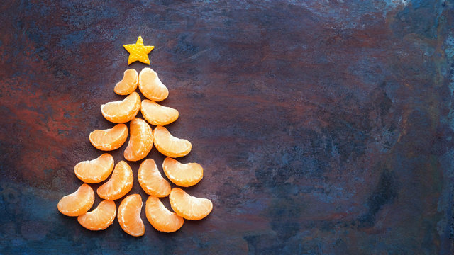 Tangerine christmas tree  on dark rust metal grunge background. Xmas festive greeting card with a tree of orange tangerine slices and star, copy space, flat lay