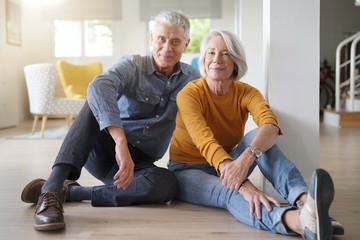  Relaxed senior couple sitting on floor in modern home looking at camera