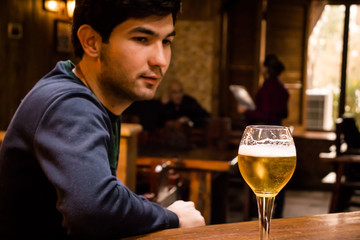 a young man at the bar looking at his glass of beer. On the blurred  background a waitress serving clients. Vintage pub atmosphere.