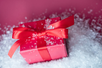 Small gift with red bow in snow on red background. Free space for your text.