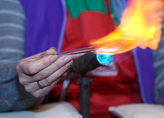 Making Christmas decorations. Glassblower’s hand warming glass blank with a gas burner