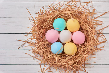 Colorful easter eggs in paper nest on a white background, top view. Easter decorations