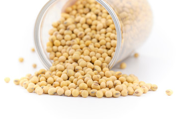 Soybeans is poured out of a glass jar and spread at on white background.