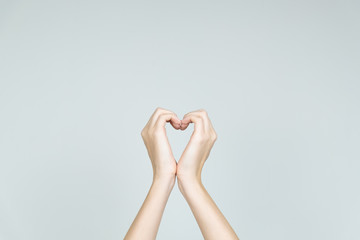 Love and kindness concept: hands forming the shape of heart. Heart formed of female hands in neutral background