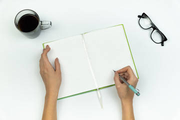 Creating new ideas concept. Top view of female hands writing in a copy book on white table