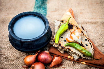 Close up of meal or lunch of villager or a typical farmer on gunny bag's background consisting of pearl millet's roti or chapati or bajra or bajri ki roti with some onions and chilies, buttermilk .