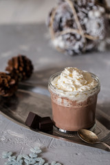 Sweet hot chocolate with cream and slice of dark chocolate in glass on tray at concrete background