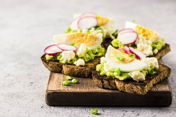 Avocado radish eggs bruschetta on cutting board. Selective fcous, space for text.