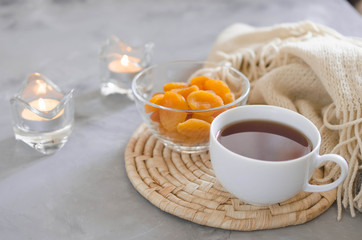 Cup of tea and dried apricots on a table, candles and knited blanket.