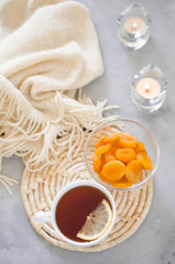 Cup of tea and dried apricots on a table, candles and knited blanket.