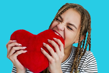 Teen girl bites red plush heart. Face with white teeth and pigtails.