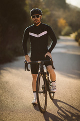 Professional road bicycle racer posing. Men cycling mountain road bike at sunset.