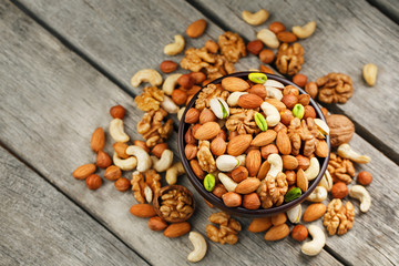 Wooden bowl with mixed nuts on a wooden gray background. Walnut, pistachios, almonds, hazelnuts and cashews, walnut.