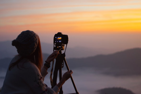 Young woman photographer taking picture of landscape when sunrise  at mountain peak.Travel and hobbies concept