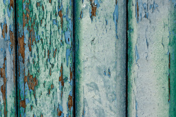 Old wooden boards painted with several layers of blue and green paints. The paint has peeled and faded from time to time.