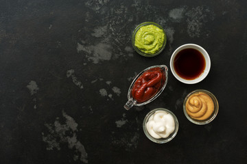 Set of various sauces in bowls on a black stone background. Mustard sauce, tomato, wasabi, mayonnaise, soy. Top view, copy space.