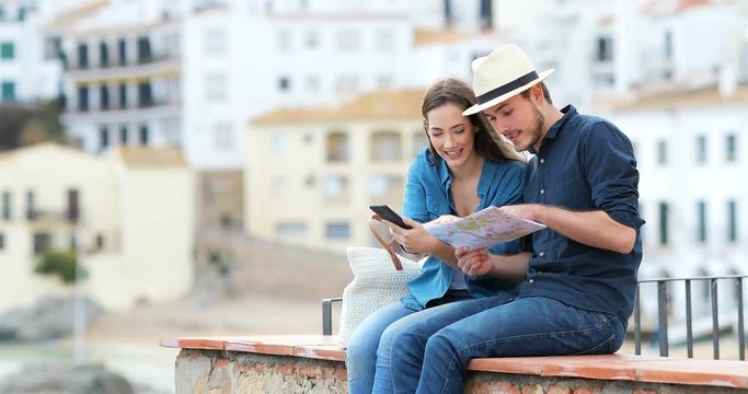 Couple of happy tourists comparing smart phone content and paper map in a coast town