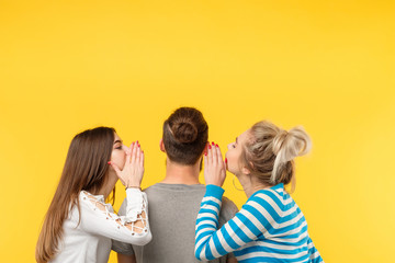 Back view of young teenage women whispering secrets to a man on yellow background