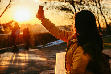 young pretty woman taking picture on her phone on sunset