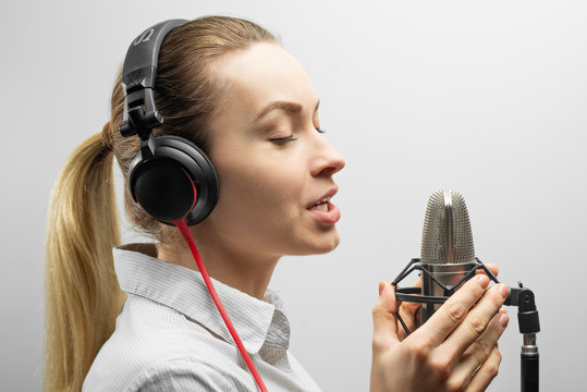 Young Beautiful Girl Writes Vocals, Radio, Voiceover Tv, Reads Poetry, Blog, Podcast In Studio On Studio Microphone In Headphones On White Background