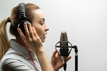 Female vocal recording. Young girl with microphone and headphones in recording studio. Recording of vocal, blogger, reading text, voice acting. - obrazy, fototapety, plakaty