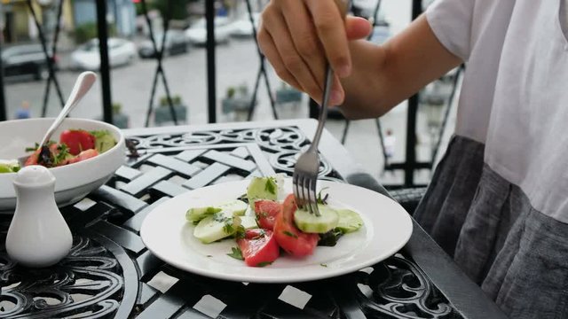 Slim woman eating vegetable salad with a fork in an outdoor restaurant