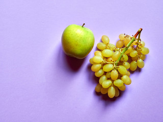 Above view of isolated set of a green apple with a bunch of sweet seedless grapes in studio with pastel violet background