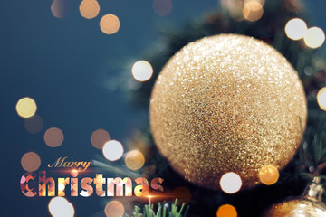 Closeup of gold bauble hanging from a decorated Christmas tree. Shiny happy new year concept with marry christmas text