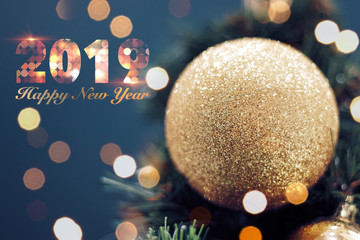 Closeup of gold bauble hanging from a decorated Christmas tree. Shiny happy new year concept with 2019 happy new year text