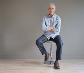  Full length casual senior man sitting on stool on gray background - Powered by Adobe