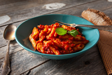 Green plate with bolognese macaroni, mint leaves, bread and spoon and fork on white rustic table top view