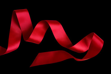 Shiny decorative red satin ribbon on black background, isolated. Scarlet tape, design element.