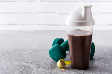 Chocolate protein shake and dumbbells on gray stone. Copyspace

