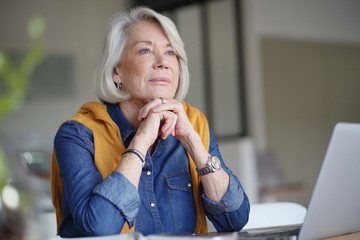  Beautiful senior woman looking pensive at home with laptop