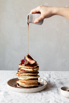 Woman pouring caramel syrup on pancakes stack