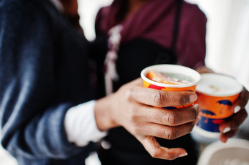 Hands of two african american woman wear on sweaters with cups of tea.