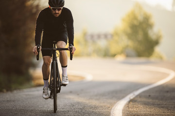 Professional road bicycle racer in action. Men cycling mountain road bike at sunset. - obrazy, fototapety, plakaty