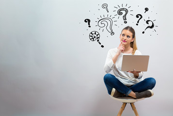 Question marks with young woman using her laptop on a grey background