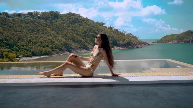 dolly shot of beautiful woman resting on the edge of swimming pool on the luxury villa