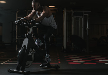 Serious black man on exercise bike in gym